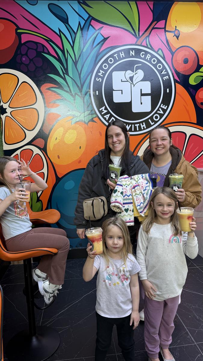 A family with kids holding Smooth N Groove drinks in front of the fruit mural