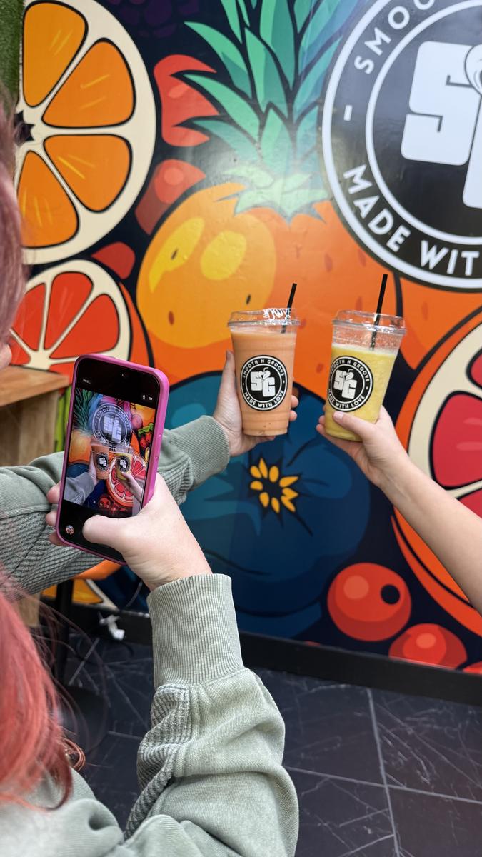 A guest photographing two Smooth N Groove cups in front of the fruit mural